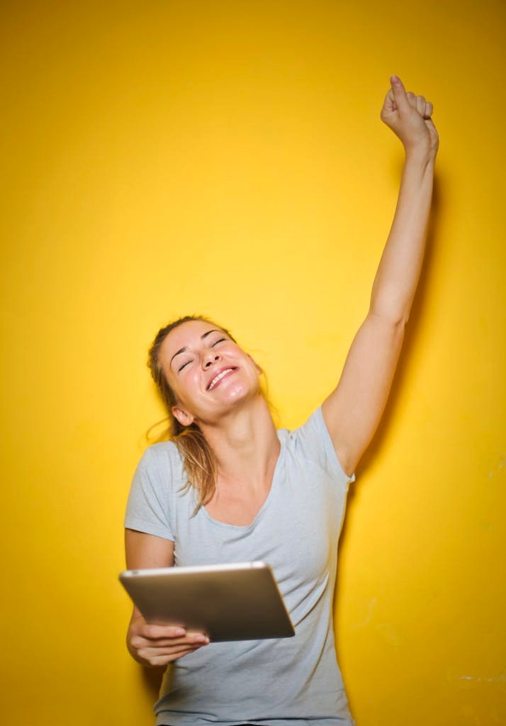 Happy woman with a tablet, celebrating success with arm raised, yellow background.
